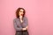 Portrait of cute pensive lady with curly hair and makeup on pink background, looks away at copy space and thinks. Thoughtful girl