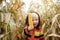 Portrait of cute playful smiling child in colorful knitted sweater playing with fresh corn cob on autumn cornfield. Childhood,