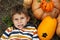 Portrait of cute preschool boy, lies on grass next to pumpkins and makes faces. Happy Halloween