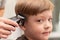 Portrait of a cute preschooler boy whose female hands are cut with a hair clipper. look into the camera. selective focus