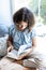 Portrait of a cute pretty teenage girl. The girl sits on the windowsill and reads a book. Soft focus. Vertical shot. Ideas home