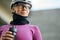 Portrait of cute professional female cyclist wearing pink suit and neck warmer looking away, holding water bottle while