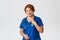 Portrait of cute redhead female doctor, nurse or physician in blue scrubs checking on patient with stethoscope, treating