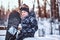 Portrait of a cute schoolboy dressed in snowsuit sitting with a snowboard on a bench at the winter forest