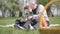 Portrait of cute senior man sitting with his grandson on the blanket in the park, looking in cellphone. The child