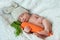Portrait of cute sleeping newborn baby boy wearing rabbit hat with ears and holding knitted carrot.