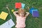 Portrait of cute smart clever school boy nerd doing homework, lie on grass.