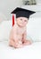 Portrait of cute smiling toddler boy in university graduation cap looking in camera