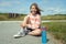 Portrait of cute teenage girl with beautiful smile sitting on ground in sneakers with blue bottle of water