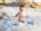 Portrait of cute toddler boy playing and having fun with lots of soap foam the beach disco party