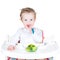 Portrait of a cute toddler eating broccoli in a white high chair