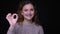 Portrait of cute young brunette wavy-haired student makes ok sign to show everything good on black background.