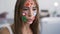 Portrait of cute young woman with painted social media icons on her face talking with her friend using camera on her