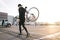 Portrait of a cyclist`s back carrying a bicycle on the background of parking at sunset