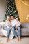 Portrait of dad, mom and son sitting on the floor at home near the Christmas tree, all are smiling. Denim and white