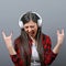 Portrait of dancing urban woman with headphones and rock on gesture with hands against gray background