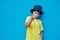 Portrait of defiant boy in yellow t-shirt and hat doing, on blue background. Copy space