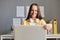 Portrait of delighted smiling attractive woman with brown hair working on laptop, sitting in front of monitor, typing on keyboard