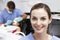 Portrait Of Dental Nurse With Dentist Examining Patient In Background