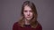 Portrait of depressed young female student watching miserably into camera on gray background.