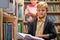 portrait of diligent caucasian child boy with book between bookshelves in campus library