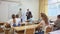 Portrait of diligent teenager schoolboy answering at board to teachers question in front of group of students in