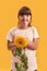 Portrait of disabled girl with Down syndrome smiling at camera while posing with sun flower isolated over yellow