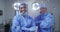 Portrait of diverse male and female surgeon wearing lowered face masks smiling in operating theatre