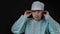 Portrait of a doctor surgeon who sits at a table and adjusts his hat and goggles on a black background.