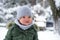 Portrait of Down syndrome toddler boy in a winter outfit, a warm grey scarf in a green jacket enjoys the frosty winter weather