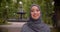 Portrait of dreamy muslim student in hijab smiling into camera standing in front of the fountain.