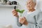 Portrait of elderely grey haired woman examining young plant at home