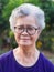 Portrait of an elderly Asian woman with short gray looking to the camera while standing in a garden. Space for text.