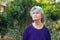 Portrait of an elderly Asian woman with short gray looking up while standing in a garden. Space for text. Concept of aged people