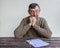 Portrait of elderly man sitting at table with white sheet of paper, pen and glasses