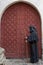 Portrait of an elderly monk 45-50 years old with a beard and a black cassock, knocking with a staff on closed old textured doors.