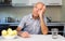 Portrait the elderly positive man sits at table in kitchen