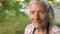 Portrait of an elderly woman in a kerchief. The wind wavers her gray hair, she looks into the camera and blinks