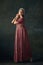 Portrait of elegant woman in image of medieval maid, wearing vintage costume against dark vintage background