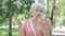 Portrait of embarrassed senior woman talking on the phone in sunny park. Confused Caucasian retiree gesturing and