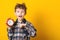 Portrait of emotional boy with alarm clock. Isolated over yellow