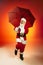 Portrait of emotional Santa Claus with umbrella jumping isolated on red yellow background in neon. Merry Christmas