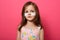 Portrait of emotional upset female child posing isolated over rose background, has white patches under eyes, standing with serious