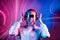 Portrait of emotionally shouting woman in futuristic sunglasses and headphones in pink and blue neon light. Music lover