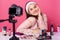 Portrait of energetic popular influencer in beauty sphere, sitting at table, making new video for blog, having lot of cosmetics on