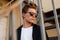 Portrait of a European serious young man with a fashionable hairstyle in stylish clothes in trendy sunglasses. Handsome guy