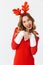 Portrait of european woman 20s wearing Santa Claus red costume and deer ears smiling and standing, isolated over white background