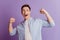 Portrait of excited astonished winner guy raise fists open mouth on purple background