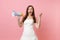 Portrait of excited bride woman with opened mouth in wedding dress holding megaphone, spreading hands on pink
