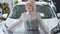 Portrait of excited Caucasian senior woman touching new vehicle, crossing hands and smiling at camera. Confident